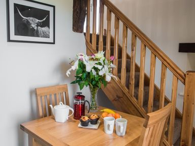 A wooden dining table with two chairs a vase of flowers a teapot a French press muffins fruit and mugs next to a wooden staircase at The Hidden Place in Watermillock near Pooley Bridge