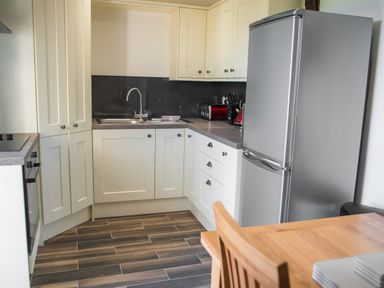 A kitchen with white cabinets a stainless steel refrigerator and sink a wooden table and chair at The Hidden Place in Watermillock near Pooley Bridge