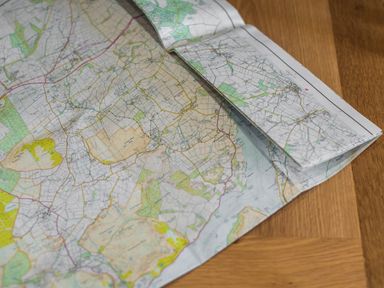 A folded paper map on a wooden surface showing roads fields and geographical details at The Hidden Place in Watermillock near Pooley Bridge