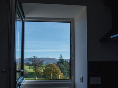 A kitchen window open to show a countryside view with trees and hills at The Hidden Place in Watermillock near Pooley Bridge