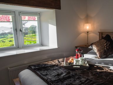 A bedroom with a bed a window looking outside a lamp on a side table and breakfast tray on the bed at The Hidden Place in Watermillock near Pooley Bridge