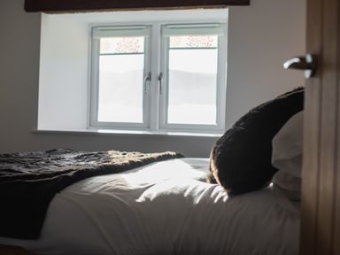 A bedroom with a bed covered by a dark blanket near a window at The Hidden Place in Watermillock near Pooley Bridge