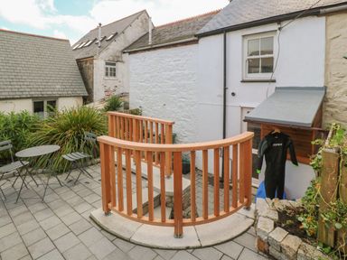 An outdoor patio area with a round table and chairs plants wooden railing and wetsuit hanging at Bodillys Cottage in Newlyn