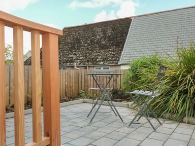 An outdoor patio with a metal table and two chairs next to a wooden fence and greenery at Bodillys Cottage in Newlyn