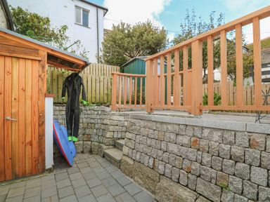 An outdoor area with a wooden shed stone retaining walls a wetsuit hanging and a blue bodyboard at Bodillys Cottage in Newlyn