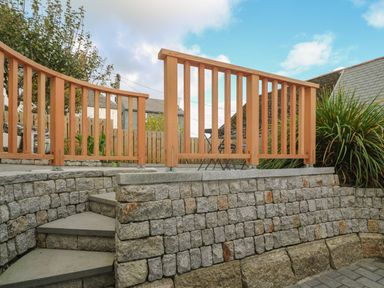 A stone retaining wall with concrete steps and a wooden railing enclosing an outdoor area at Bodillys Cottage in Newlyn