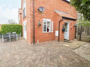 A brick house exterior with a white door open and a window open patio furniture and greenery at 30 Burtons Mill in Stalham