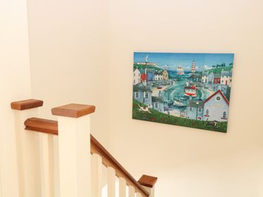 A staircase with wooden handrails and a painting of a seaside village on the wall at 30 Burtons Mill in Stalham