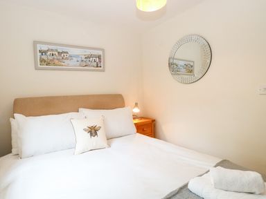 A bedroom with a bed a bedside table with lamp a round mirror and a framed picture above the bed at 30 Burtons Mill in Stalham