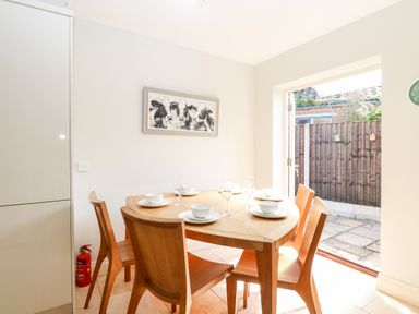 A dining area with wooden table and chairs set with bowls and glasses next to an open door showing a fenced patio at 30 Burtons Mill in Stalham