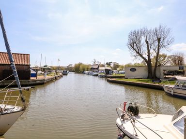 A river with boats docked along the banks and bare trees at 30 Burtons Mill in Stalham