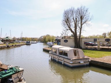 A canal with boats docked along the sides and a tree near a small building at 30 Burtons Mill in Stalham