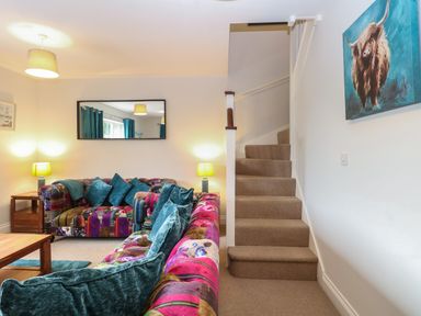 A living room with patchwork sofas and teal cushions next to carpeted stairs at 30 Burtons Mill in Stalham