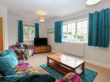 A living room with a wooden coffee table teal curtains and a colorful sofa at 30 Burtons Mill in Stalham