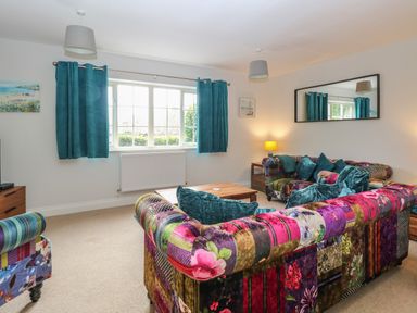 A living room with patchwork sofas teal curtains a wooden coffee table and a wall mirror at 30 Burtons Mill in Stalham