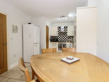 A kitchen with a wooden dining table and chairs a white refrigerator and cabinets with a checkered backsplash at 30 Burtons Mill in Stalham