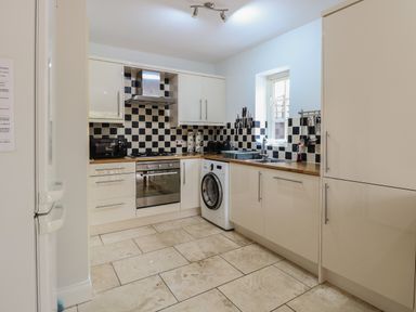 A kitchen with white cabinets black and white checkered backsplash a washing machine oven and a window at 30 Burtons Mill in Stalham