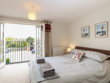 A bedroom with a double bed towels and pillows on the bed and an open balcony door at 30 Burtons Mill in Stalham