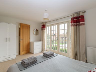 A bedroom with a bed folded towels on it a white wardrobe a white chest of drawers and large windows with curtains at 30 Burtons Mill in Stalham