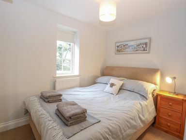 A bedroom with a double bed two sets of folded towels a wooden bedside table with a lamp and a window at 30 Burtons Mill in Stalham