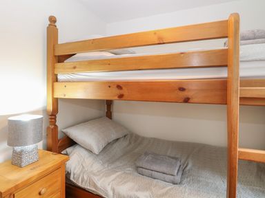 A bedroom with wooden bunk beds a nightstand with a lamp and folded towels on the bed at 30 Burtons Mill in Stalham