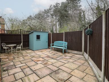 A paved backyard with a blue garden shed a turquoise bench and a white metal table with two chairs at 30 Burtons Mill in Stalham
