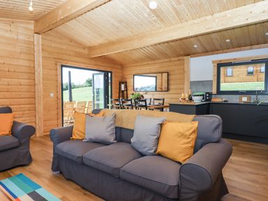 A living area with gray sofas and cushions next to a dining table and open doors to outside at Primrose Lodge in Hittisleigh