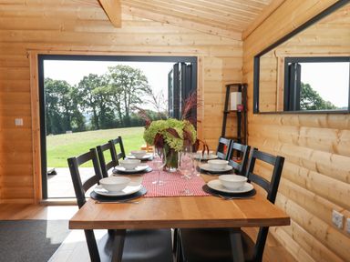 A dining table with plates bowls glasses and a flower centerpiece in a wooden room at Primrose Lodge in Hittisleigh