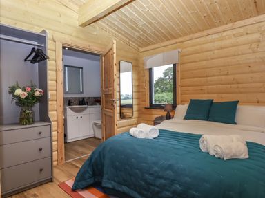 A bedroom with a double bed blue bedding and towels a dresser with flowers an open door to a bathroom at Primrose Lodge in Hittisleigh