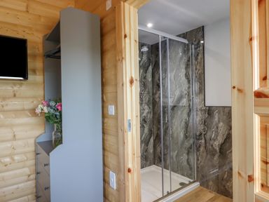 A bathroom with a glass shower enclosure and grey marbled walls next to a wooden wall with a grey wardrobe cabinet and a vase with flowers at Primrose Lodge in Hittisleigh