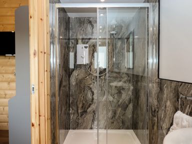 A bathroom with a glass shower enclosure and marble patterned walls at Primrose Lodge in Hittisleigh