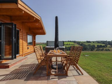 A wooden patio table with chairs and breakfast set outside a wooden house with countryside view at Primrose Lodge in Hittisleigh