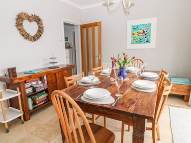 A dining room with a wooden table set for six with plates wine glasses a vase of flowers and a bottle of prosecco at Looe Island View in Downderry