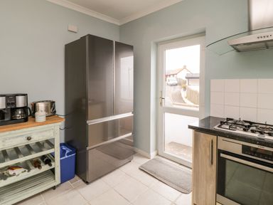 A kitchen with a stainless steel refrigerator a wooden cart with a coffee maker and toaster a gas stove and an oven next to a door with a window at Looe Island View in Downderry