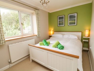 A bedroom with a bed with white and green towels on it two framed pictures on a green wall two bedside tables with lamps and a window with curtains at Looe Island View in Downderry