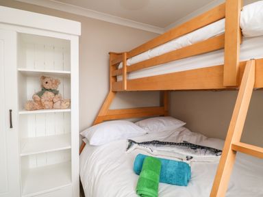 A bunk bed with white bedding and pillows a stuffed fish and two rolled towels near a white cabinet with a teddy bear inside at Looe Island View in Downderry