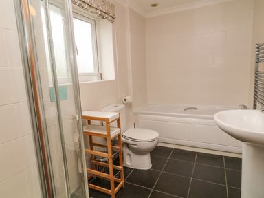 A bathroom with a shower, toilet, bathtub, sink, window, and wooden storage unit at Looe Island View in Downderry