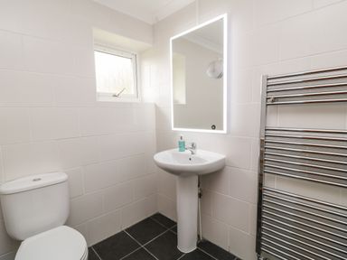 A bathroom with a toilet, pedestal sink with hand soap, illuminated rectangular mirror, window, and heated towel rail at Looe Island View in Downderry