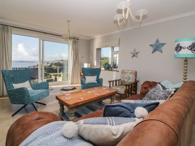 A living room with a brown sofa blue armchairs a wooden coffee table with playing cards and a sea view at Looe Island View in Downderry