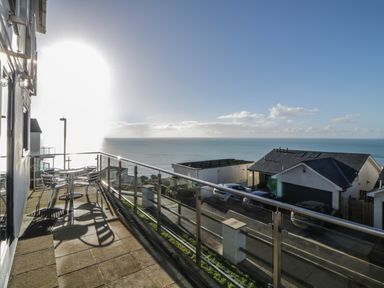 A balcony with a table and chairs overlooking the sea and neighboring houses at Looe Island View in Downderry