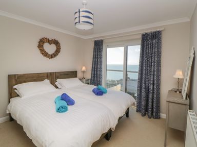 A bedroom with two single beds next to a window with blue curtains at Looe Island View in Downderry