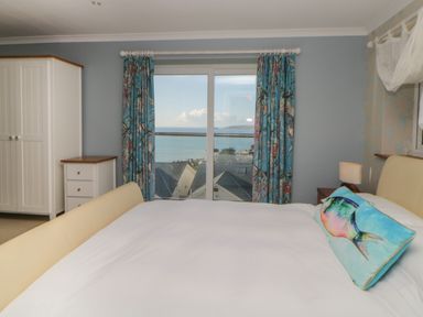 A bedroom with a bed and a decorative fish pillow a wardrobe and window with blue floral curtains overlooking a sea view at Looe Island View in Downderry