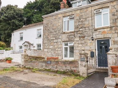 A stone house with a black door and white windows next to a white house with a gate and garden at Still Waters in Pentewan
