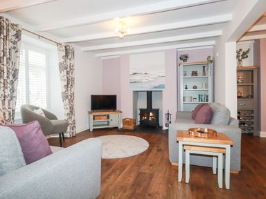 A living room with gray sofas purple cushions a fireplace television and wooden flooring at Still Waters in Pentewan