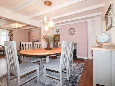 A dining room with six chairs around a wooden table a vase with flowers pendant lights a clock a globe and a cabinet at Still Waters in Pentewan