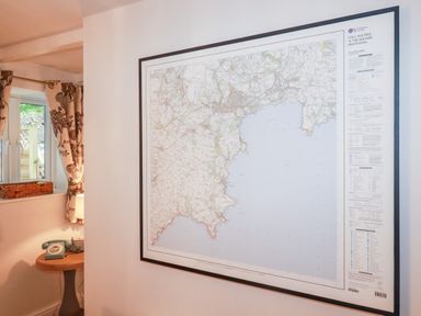 A framed map on a wall next to a side table with a green rotary phone and a lamp at Still Waters in Pentewan