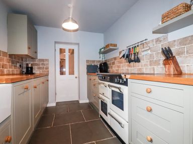 A kitchen with light gray cabinets wooden countertops a double oven stove tiled backsplash utensils hanging on the wall and a white door at Still Waters in Pentewan