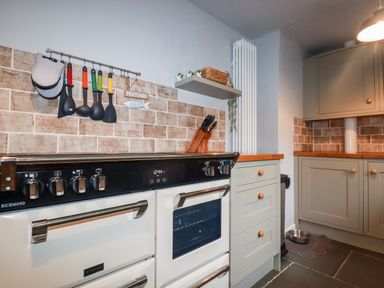 A kitchen with a white stove and oven next to light green cabinets and a knife block at Still Waters in Pentewan