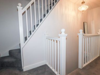 A staircase with white railing and grey carpet and a wall mirror on the side at Still Waters in Pentewan