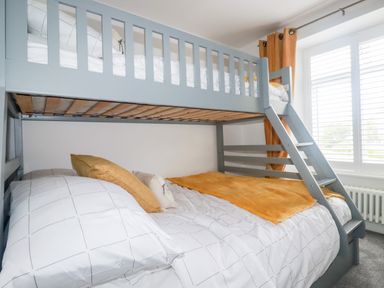 A bedroom with a gray bunk bed and pillows next to a window with orange curtains at Still Waters in Pentewan